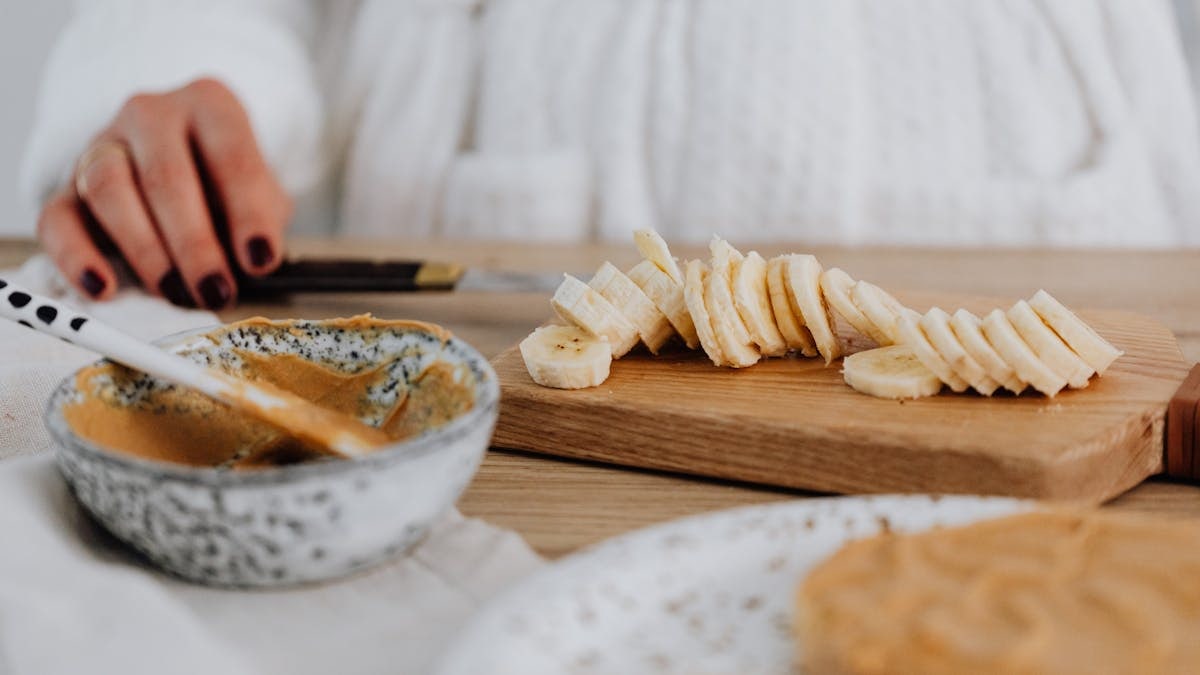 Close-up of sliced bananas on a wooden board with peanut butter in a bowl.