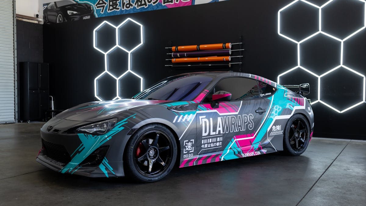 Dynamic photo of a sleek sports car with colorful custom vinyl wrap by DLA Wraps in a shop setting.